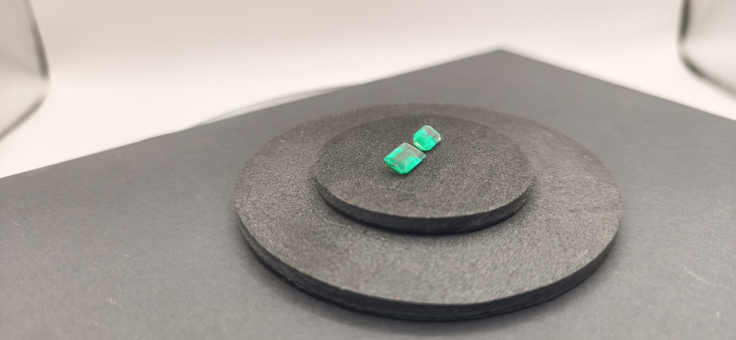 Two emeralds of identical carat weight but different face-up dimensions due to cut proportions