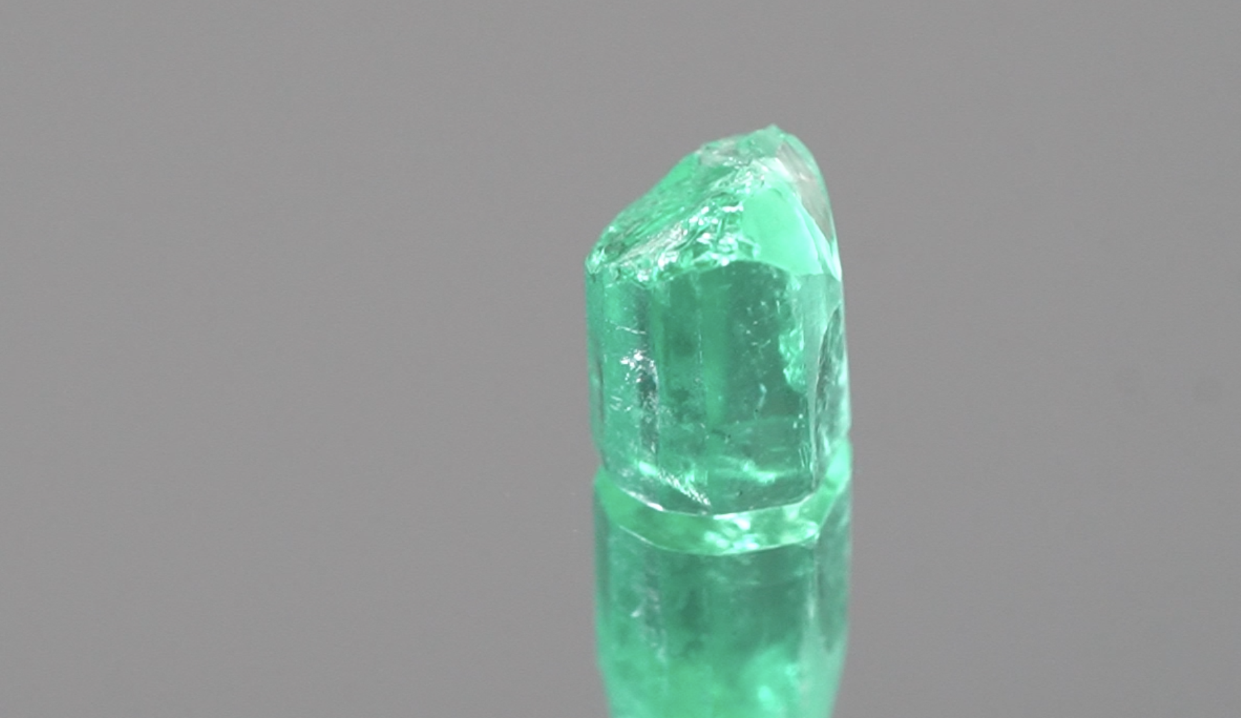 Rough emerald crystal next to finished cut stones showing the transformation from rough to faceted gem